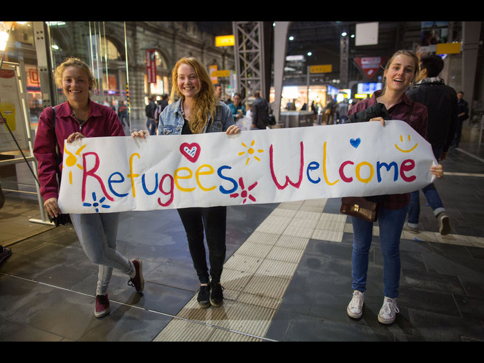 Drei junge Frauen stehen am 05.09.2015 in Frankfurt am Main (Hessen) im Hauptbahnhof mit einem Begrüßungsplakat mit der Aufschrift "Refugees Welcome" für Flüchtlinge an den Gleisen. Foto: Frank Rumpenhorst/dpa +++(c) dpa - Bildfunk+++ urn:newsml:dpa.com:20090101:150906-90-001226